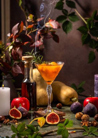 Smoking orange cocktail is garnished with rosemary and surrounded by autumnal fruits, nuts, and candles, evoking warmth and festivityの写真素材