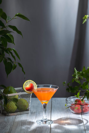 Vibrant orange cocktail is garnished with a fresh strawberry and lime slice, creating a refreshing summer drinkの写真素材