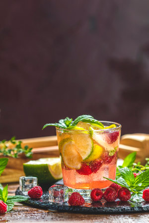 Glass of vibrant pink raspberry lemonade infused with citrus fruits, ice, and fresh mint, creating a refreshing summer beverageの写真素材