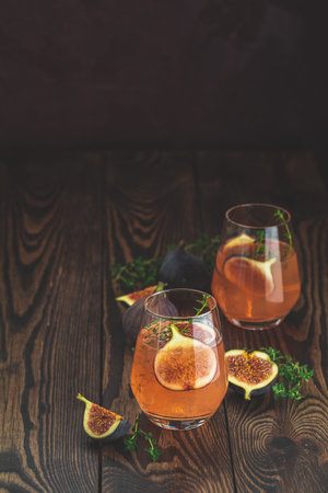 Two refreshing pink cocktails garnished with fresh figs and thyme sprigs sit on a dark wooden table, creating a vibrant and inviting sceneの写真素材