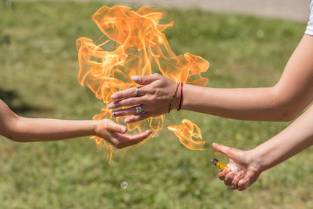 Street performer captivating an audience by confidently holding fire in hand during a sunny summer...