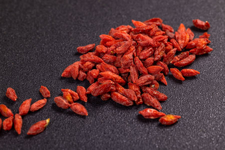 Numerous dried goji berries are scattered across a dark surface, creating a visually appealing arrangementの写真素材