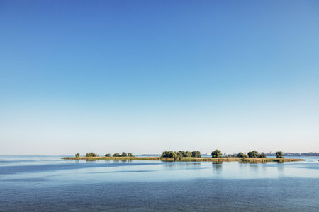 Beautiful landscape showing small islands reflecting on the calm water of a river under a clear blue...