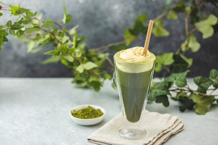 Preparing an iced matcha latte topped with whipped cream and garnished with fresh ivy branches, creating a refreshing summer drinkの写真素材