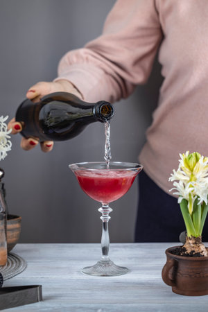 Bartender pouring sparkling wine into a cocktail glass with red liquor, ice, and flower decorations for a refreshing drinkの写真素材