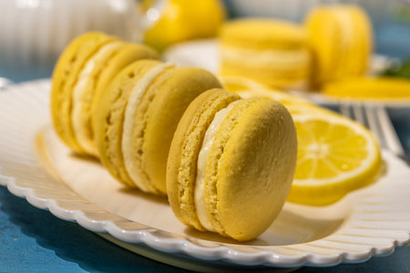 Delightful yellow lemon macarons, filled with creamy white goodness, beautifully arranged on a white plate alongside fresh lemon slicesの写真素材