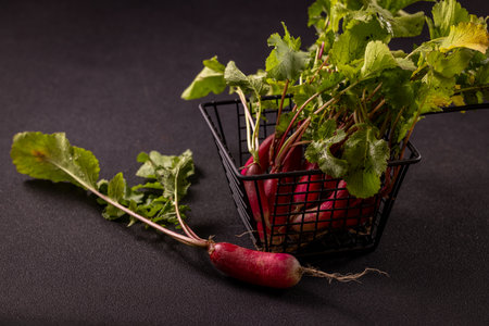 Vibrant red radishes with lush green leaves overflowing from a dark metal basket, creating an eye catching display of fresh produceの写真素材