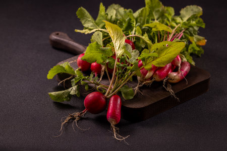Vibrant red radishes with lush green leaves are presented on a rustic wooden cutting board, creating a simple yet appealing displayの写真素材