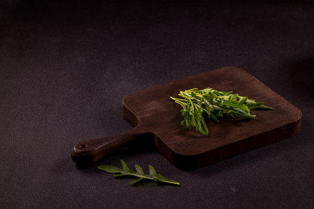 Fresh arugula leaves are placed on a rustic wooden cutting board, creating a simple yet elegant culinary sceneの写真素材