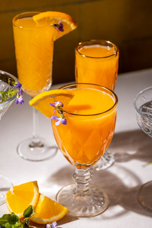 Crystal glasses filled with vibrant orange cocktails, garnished with edible flowers and orange slices, create a refreshing and visually appealing sceneの写真素材