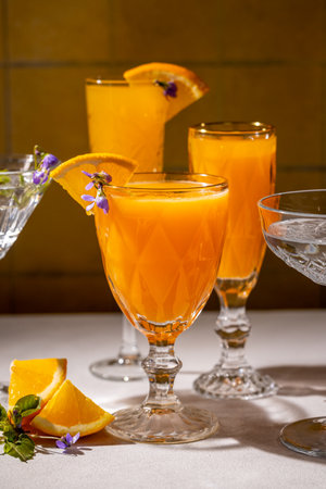 Crystal glasses filled with vibrant orange juice cocktails, garnished with edible flowers and orange slices, create a refreshing and visually appealing sceneの写真素材