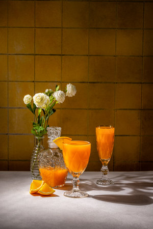 Two glasses and a crystal decanter filled with orange juice are beautifully arranged on a table with orange slices and white flowers, creating a refreshing breakfast sceneの写真素材