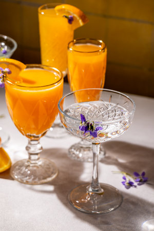 Crystal glasses containing refreshing orange juice cocktails are garnished with edible flowers and orange slices, creating a sophisticated and vibrant beverage presentationの写真素材
