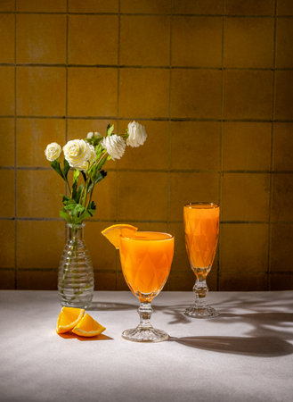 Refreshing orange juice served in elegant glasses, accompanied by orange slices and a vase of white flowers, creating a vibrant and inviting sceneの写真素材