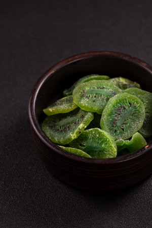 Dried kiwi slices filling a rustic brown bowl, presenting a healthy and sweet snack option on a dark background, highlighting natural patterns and vibrant green colorの写真素材