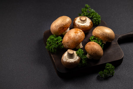 Fresh cremini mushrooms and bright parsley sprigs arranged on a rustic dark cutting board, ready for cooking or a wholesome, plant based meal preparation sceneの写真素材