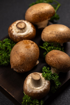 Fresh cremini mushrooms with rich brown caps and creamy stems, paired with bright parsley on a rustic dark cutting board, evoking wholesome, natural cooking and healthy eatingの写真素材