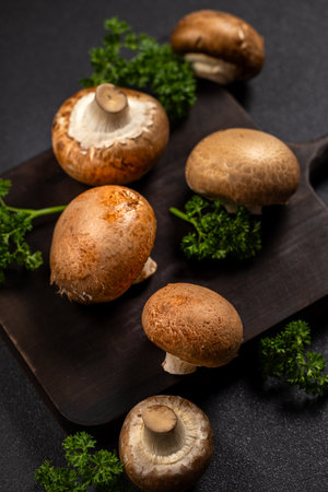 Brown cremini mushrooms and fresh green parsley leaves arranged on a rustic dark wooden cutting board, highlighting healthy organic ingredients for cookingの写真素材