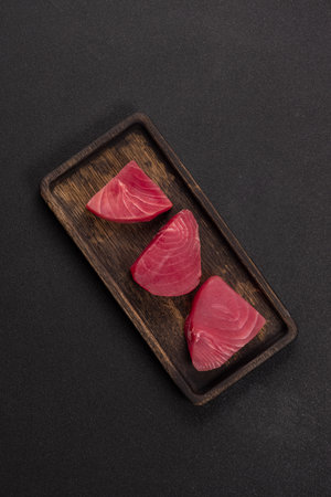 Fresh red tuna steaks, sliced and perfectly arranged on a dark wooden serving tray, ready for preparation as a healthy and protein rich seafood meal or gourmet sushiの写真素材