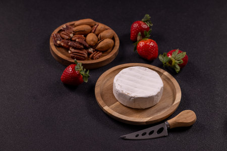 Soft white mold cheese with fresh strawberries, pecans and a cheese knife on a rustic wooden plate  elegant sweet and savory appetizer platter for entertaining and snackingの写真素材