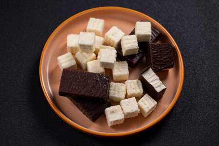 Assorted dark chocolate coated marshmallow and coconut cubes arranged on a brown plate against a black background  decadent, homemade style dessert assortment, top view closeupの写真素材
