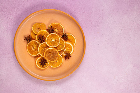 Dried orange slices and star anise on an orange plate, overhead flat lay on pink textured...