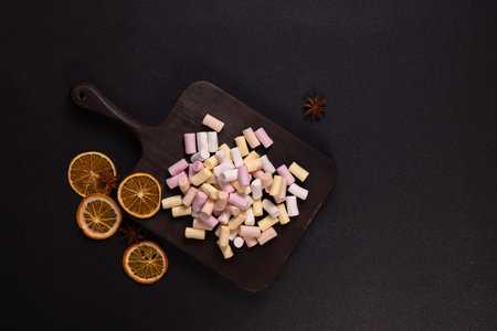 Colorful marshmallows mixing with dried orange slices and star anise on a dark wooden cutting board,...