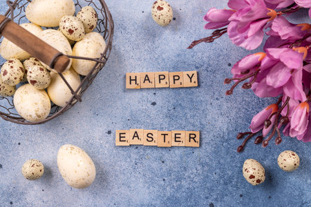 Easter eggs in a metal basket alongside speckled quail eggs and purple spring flowers, with wooden...
