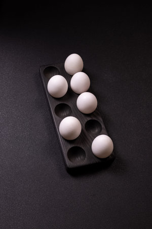White eggs resting in a stylish dark wooden holder, presented against a minimalist black background...