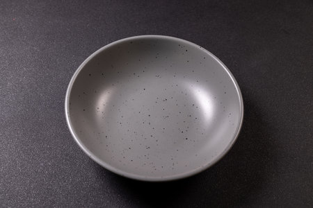 Empty speckled gray ceramic bowl on dark textured tabletop, minimalist top view studio shot with clean, neutral background and ample copy space for culinary or design useの写真素材