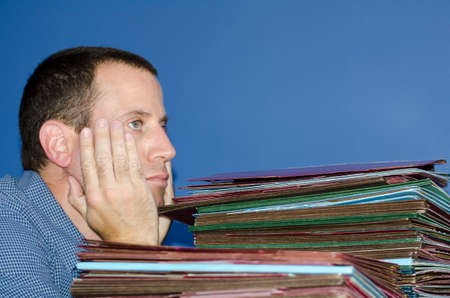 Man stressed out at work with hands on his face sitting in front of a large pile of files.の写真素材