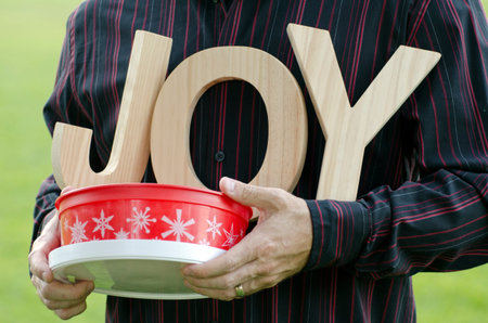 Wooden letters of the word joy - close up of man's hands holding the word with a Holiday themed red...