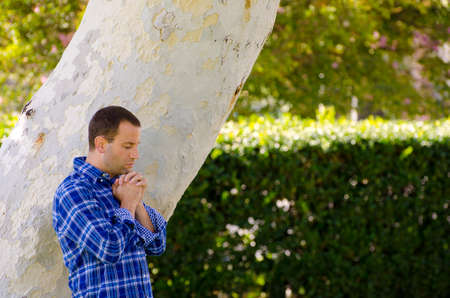Man praying in a park by a large tree trunk.の写真素材