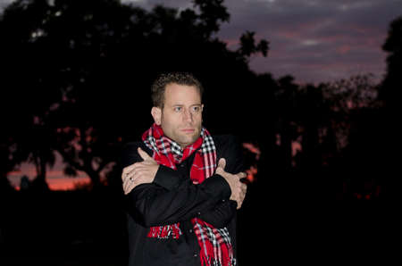 Man rubbing his arms trying to get warm at sunset wearing a black shirt and red scarf.の写真素材