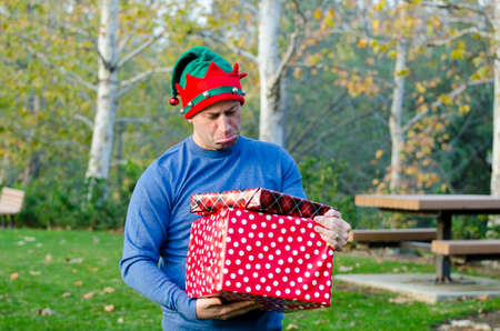 Man with sad face holding gifts outdoors wearing a blue sweater.の写真素材