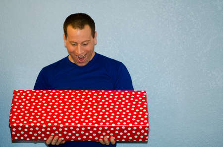 Man surprised by a large wrapped gift his is holding in his hands.の写真素材