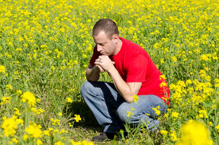 Man praying alone in a field of yellow flowers.の写真素材