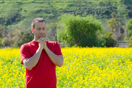 Man praying alone with his hands clasped under his chin and eyes closed.の写真素材