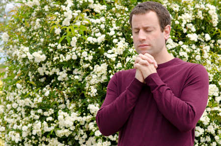 Man praying with a bush with white flowers in the background.の写真素材