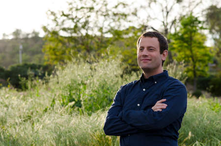 Smiling man looking forward to the future in a grassy field with arms crossed.の写真素材