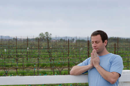 Man praying leaning on a white fence in a vineyard.の写真素材