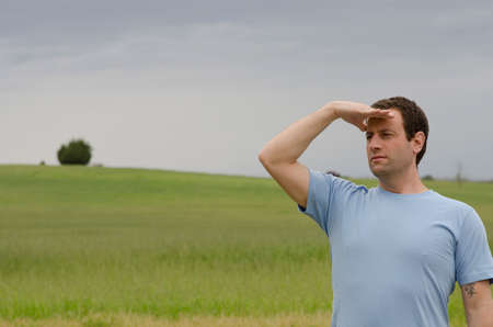 Man looking out to what the future holds in an open field of green grass.の写真素材