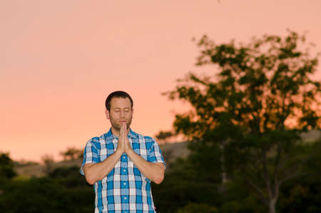 Man praying alone at dusk with pink skies in the background.の写真素材