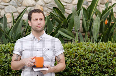 Man thinking of what tomorrow brings holding a book and coffee mug.の写真素材