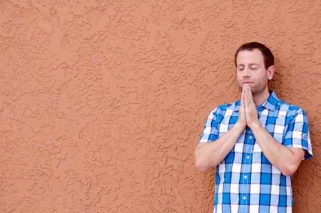 Man praying with a beige stucco wall as the background.の写真素材