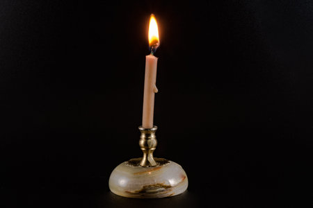 Burning candle on a stand on a black background
