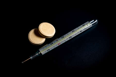 Thermometer on a black background and cold pillsの写真素材