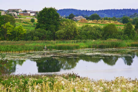 Lake water in serenity. On the beach sits a fishermanの写真素材