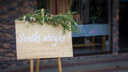 Welcome sign at the entrance of a wedding celebration dinner written in white letters on a wooden board and decorated with plantsの写真素材