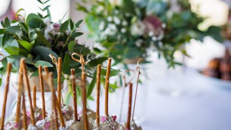 Bamboo sticks on a sweet table decorated with some green flowers and some pink rose blossomの写真素材
